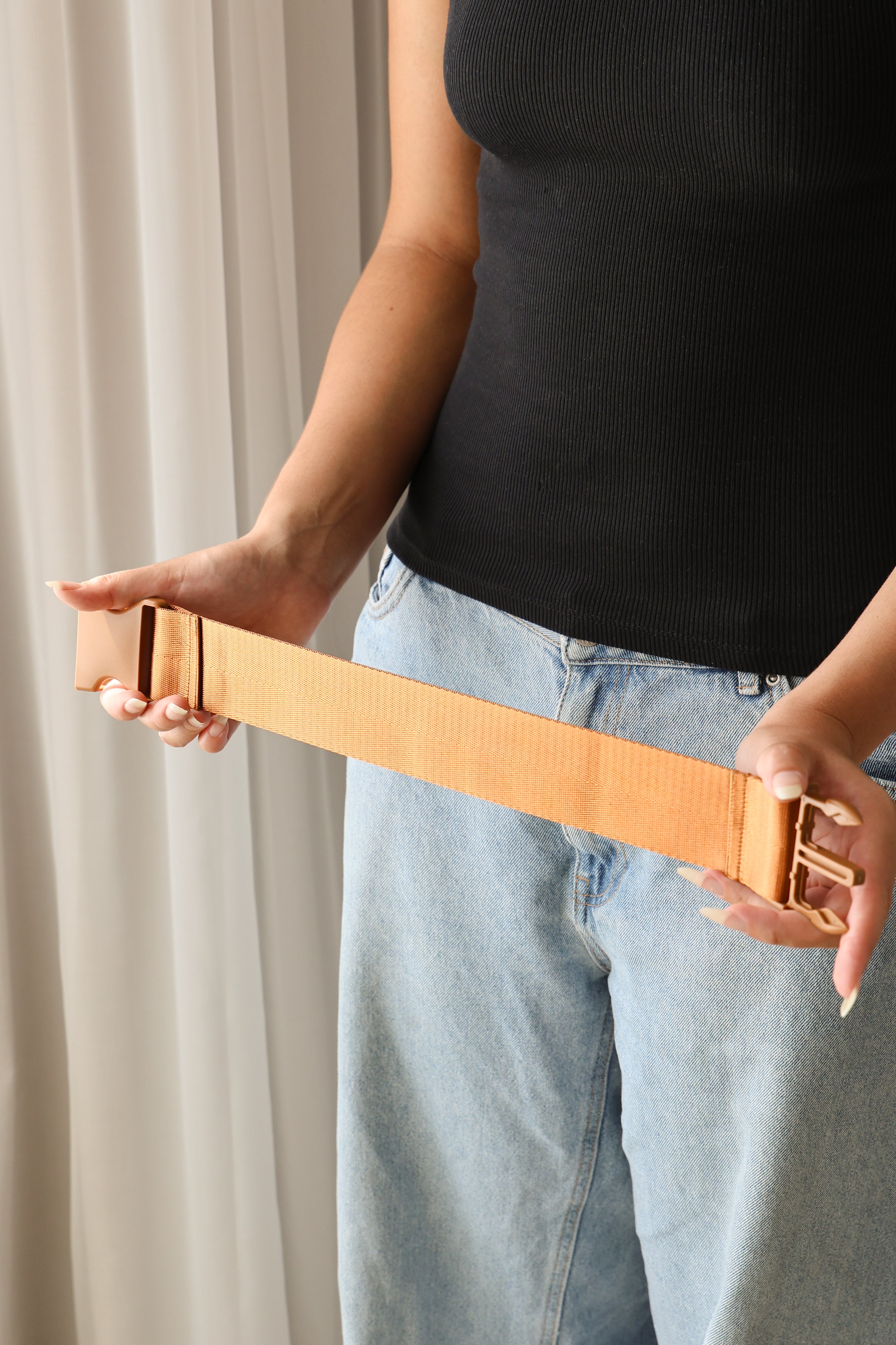 A woman holds an extended Size Extender strap in two hands. The Strap is Chekoh's signature strap colour in a golden brown, matching the buckles.