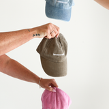 Three people holding Denim, Bone, and Pink Chekoh hat/caps against a white background to show the full range of Handsfree Mode caps available.
