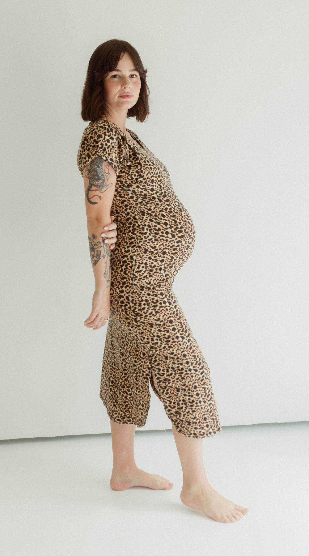 A pregnant woman wears the Chekoh Leopard print Journey Dress, standing barefoot and comfortable in a studio environment.