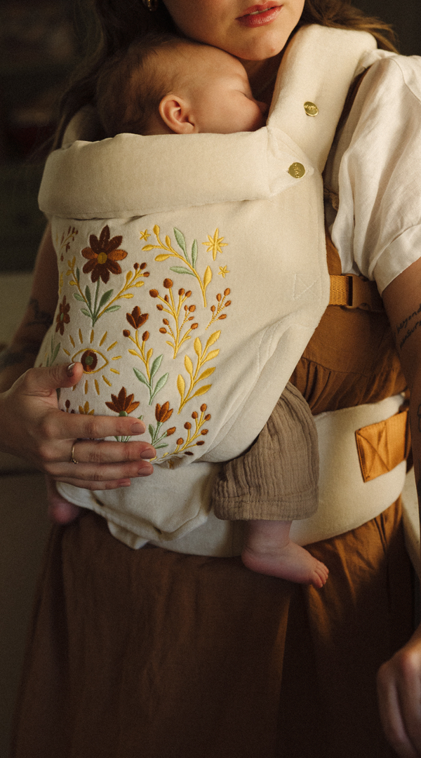 Person holding a baby in a floral-patterned Chekoh baby carrier.