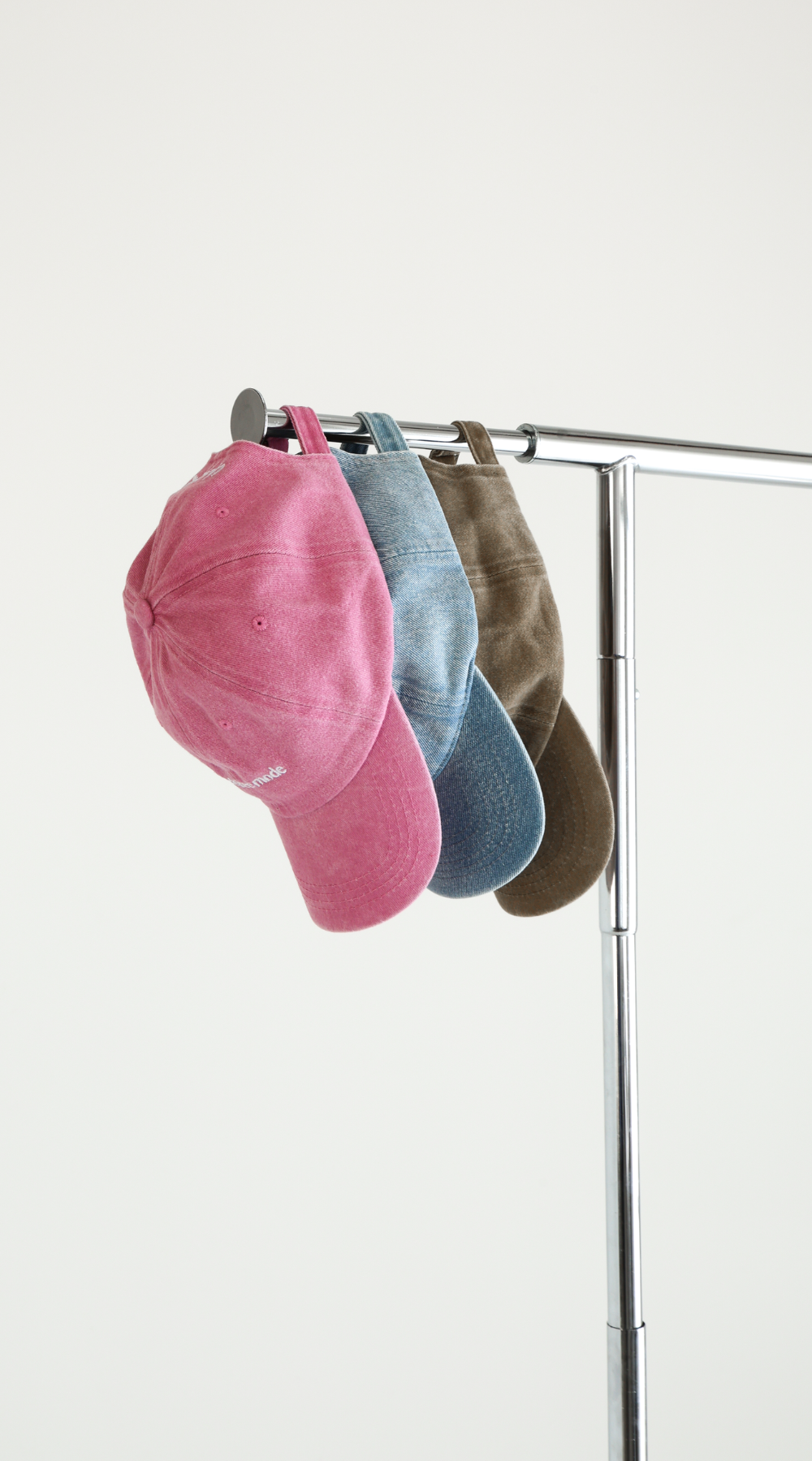 Pink, Denim and Bone Chekoh Baby Mom-Friendly Caps lined up on metal clothing rack on white backdrop.