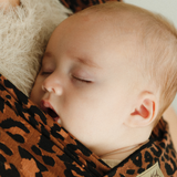Baby sleeping soundly in a Leopard Chekoh Baby Wrap - featuring colours of brown, black and deep tan. You can see the exclusive Chekoh logo under the nape of baby's neck.