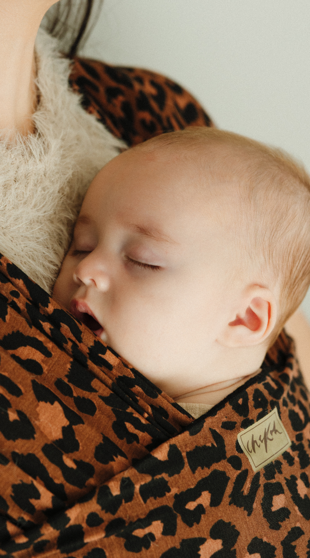 Baby sleeping soundly in a Leopard Chekoh Baby Wrap - featuring colours of brown, black and deep tan. You can see the exclusive Chekoh logo under the nape of baby's neck.