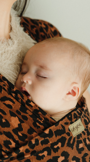 Baby sleeping soundly in a Leopard Chekoh Baby Wrap - featuring colours of brown, black and deep tan. You can see the exclusive Chekoh logo under the nape of baby's neck.