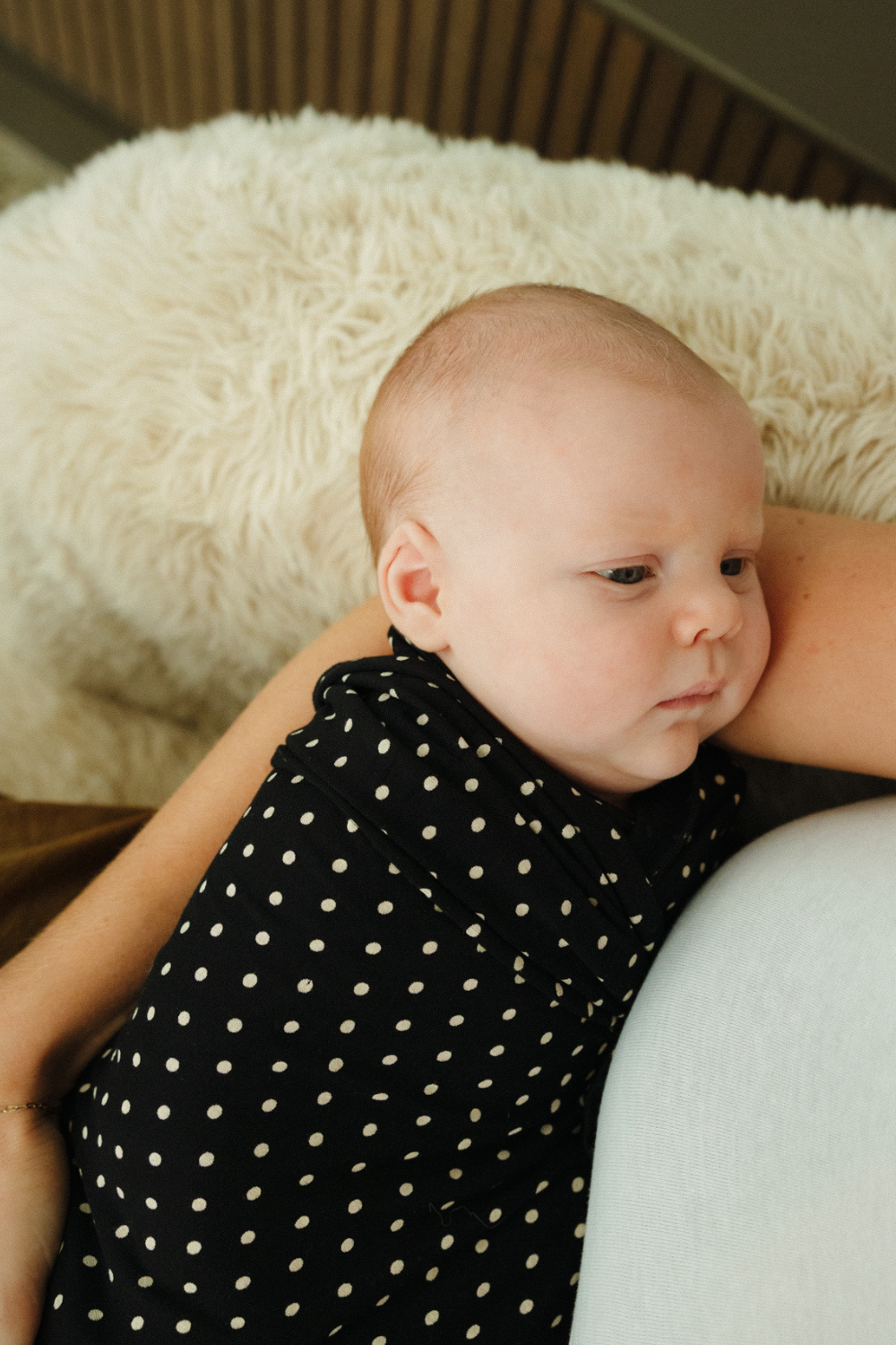 A cute newborn face looks up at mum while swaddled in a black and white polka dot print swaddle - exclusive and limited edition at Chekoh Baby