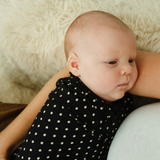 A cute newborn face looks up at mum while swaddled in a black and white polka dot print swaddle - exclusive and limited edition at Chekoh Baby
