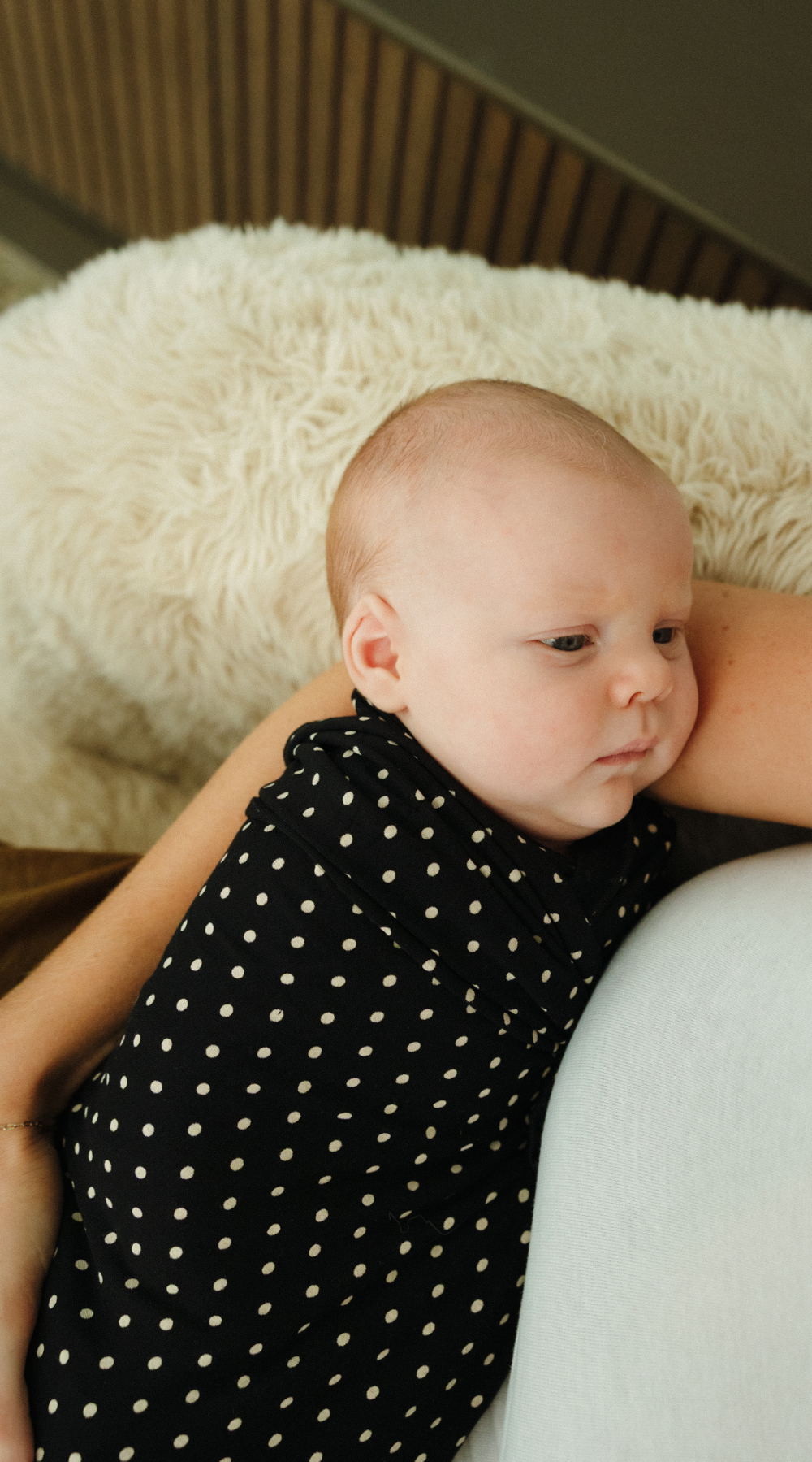 A cute newborn face looks up at mum while swaddled in a black and white polka dot print swaddle - exclusive and limited edition at Chekoh Baby