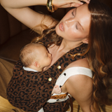Woman holding a baby in the Leopard clip Carrier 2.0 by Chekoh Baby on a wooden floor. Baby is sleeping snuggly against Mum.