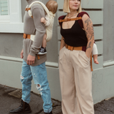 Man and woman, wearing their babies in a back carry using the Chekoh Chest Strap for added support.