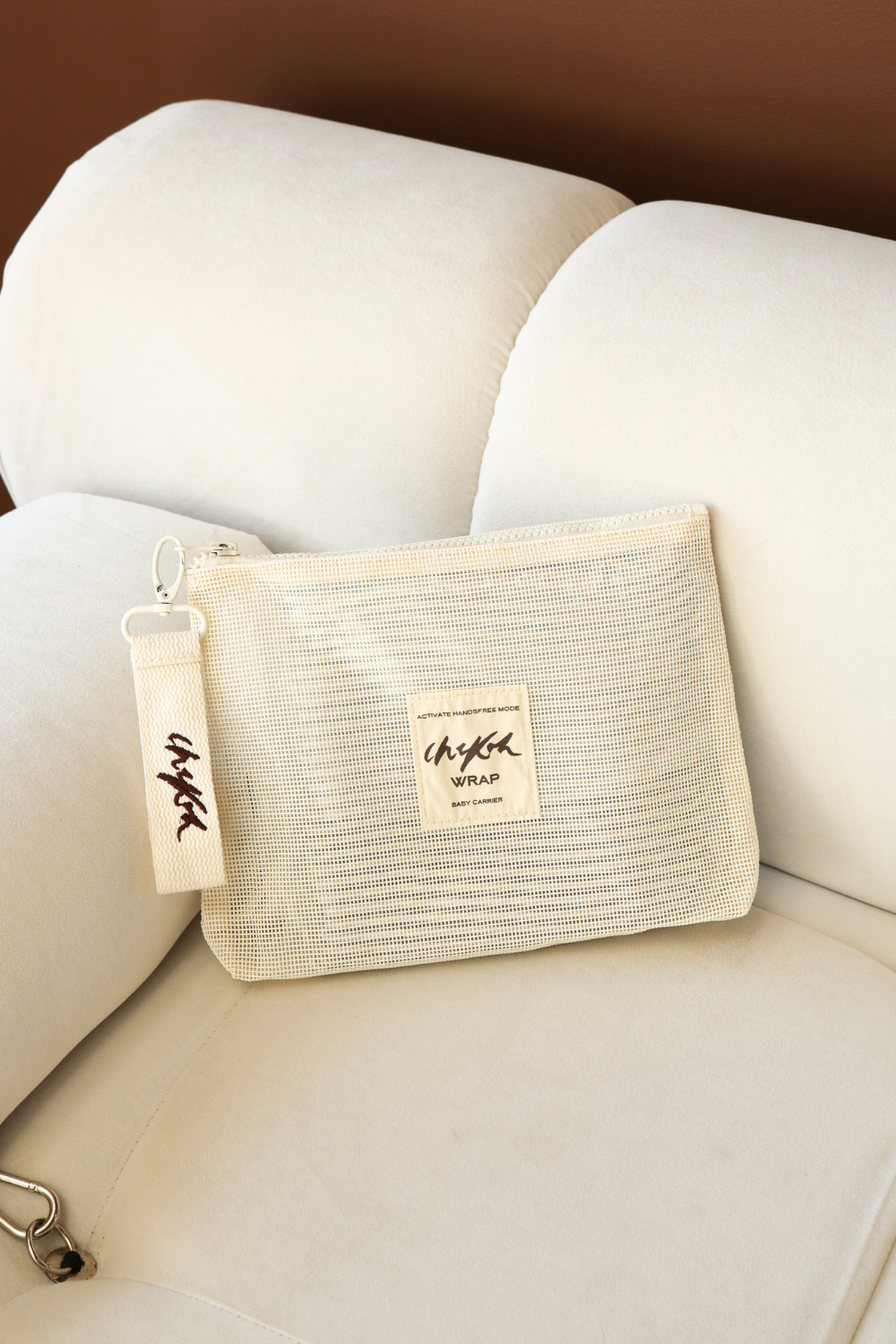 Beige Wrap Storage Bag Pouch by Chekoh Baby - sat on an off white couch in front of a brown wall.