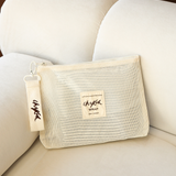 Beige Wrap Storage Bag Pouch by Chekoh Baby - sat on an off white couch in front of a brown wall.