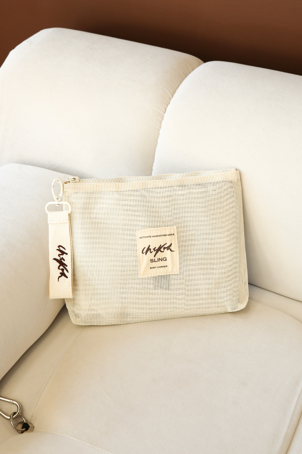 Beige Sling Storage Bag Pouch by Chekoh Baby on an off white couch with brown background.