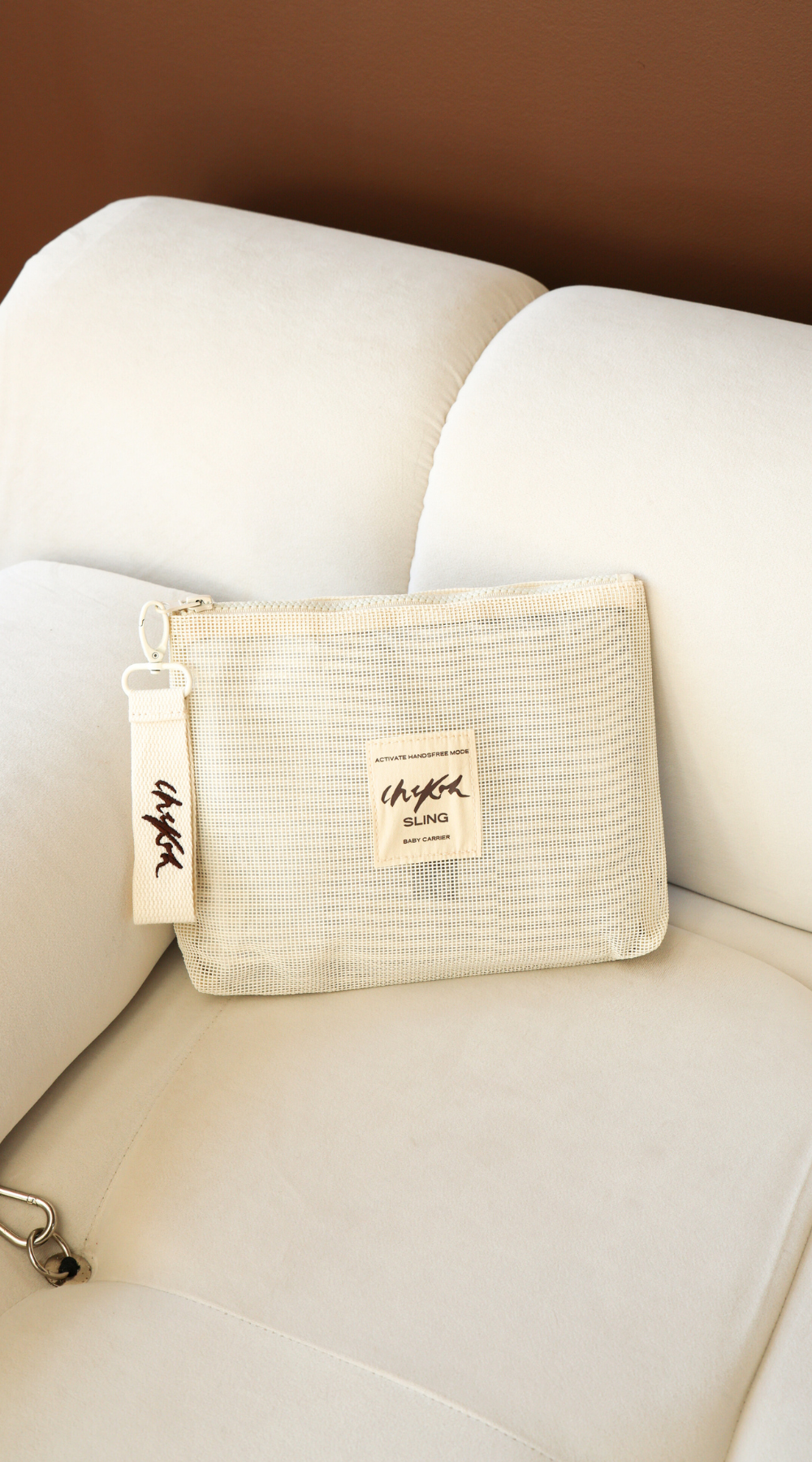 Beige Sling Storage Bag Pouch by Chekoh Baby on an off white couch with brown background.