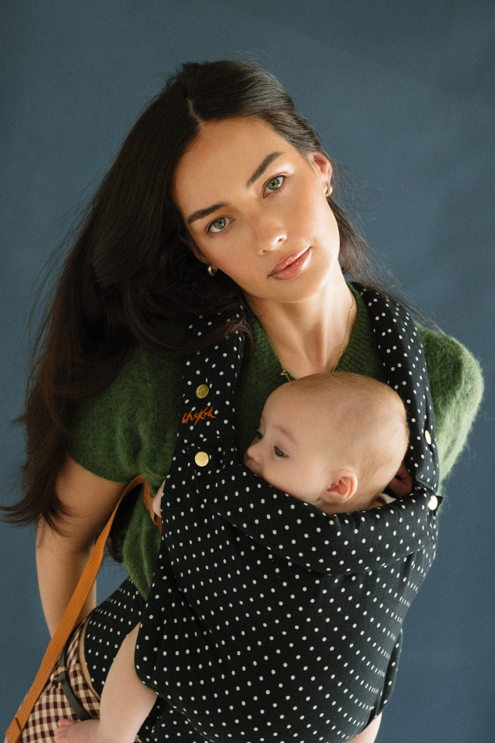 A baby is resting comfortably against mom in a Chekoh Baby Clip Carrier 2.0 - in the new limited edition and exclusive Polka Dot print.