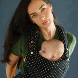 A baby is resting comfortably against mom in a Chekoh Baby Clip Carrier 2.0 - in the new limited edition and exclusive Polka Dot print.