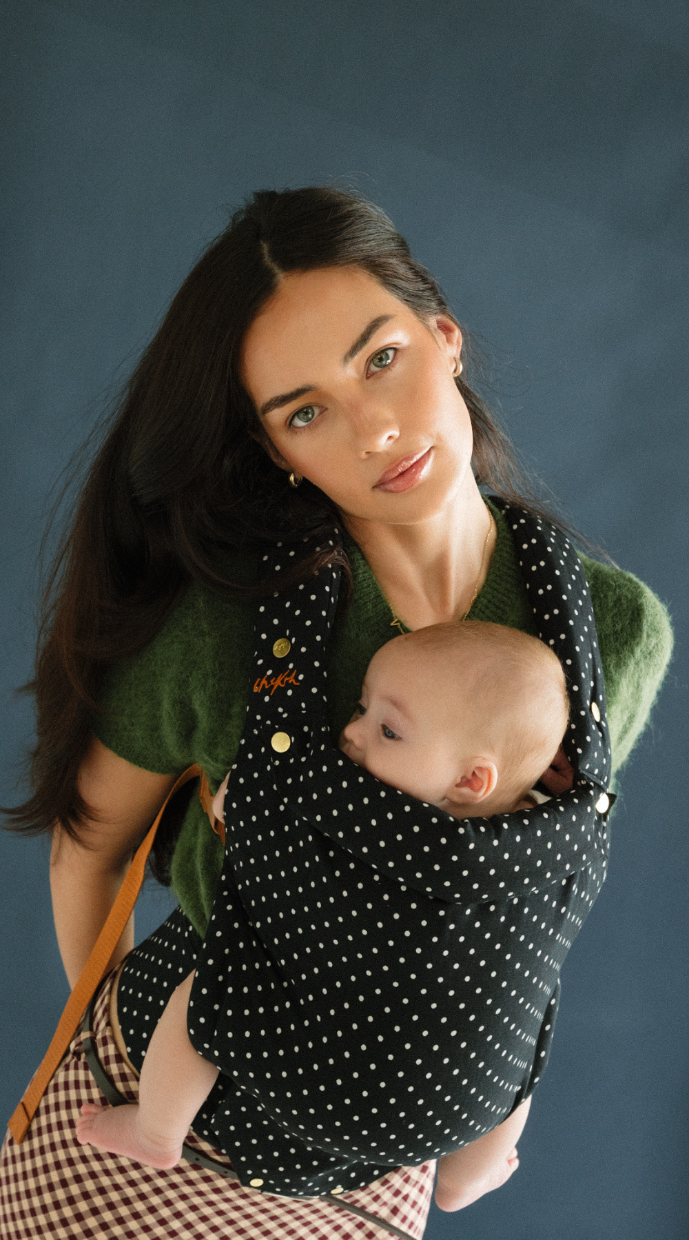 A baby is resting comfortably against mom in a Chekoh Baby Clip Carrier 2.0 - in the new limited edition and exclusive Polka Dot print.