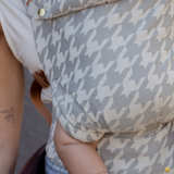 Close up detail shot of baby in the Hudson Houndstooth Clip Carrier by Chekoh. You can see the houndstooth detail in grey and off grey, as well as the gold buttons and hardware. 