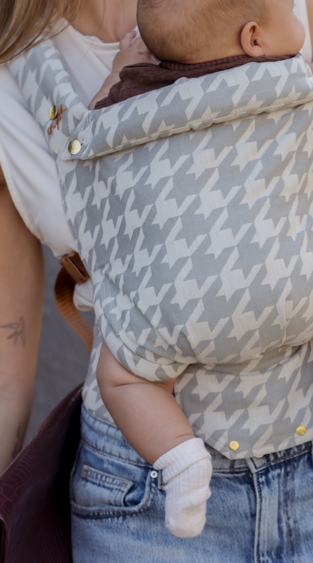 Close up detail shot of baby in the Hudson Houndstooth Clip Carrier by Chekoh. You can see the houndstooth detail in grey and off grey, as well as the gold buttons and hardware. 