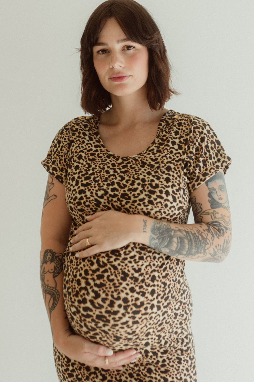A pregnant woman wearing a leopard print dress by Chekoh with short sleeves, holding her belly.
