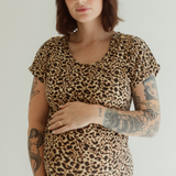 A pregnant woman wearing a leopard print dress by Chekoh with short sleeves, holding her belly.