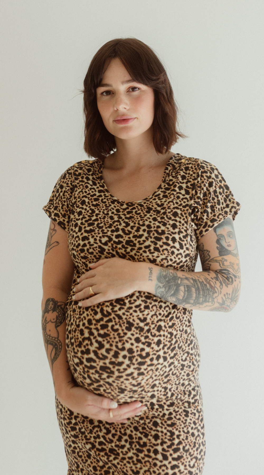 A pregnant woman wearing a leopard print dress by Chekoh with short sleeves, holding her belly.