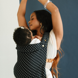 A woman holds her baby close and demonstrates that hands-free feeling you get when babywearing. She has her arms in the air and baby is looking up at her from the comfort of a Chekoh Baby Clip Carrier in Polka Dot.