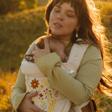 A mother and baby share a moment in a field wearing the vintage white cotton velvet Juni Clip. Featuring a stunning floral seeing eye embroidered design.