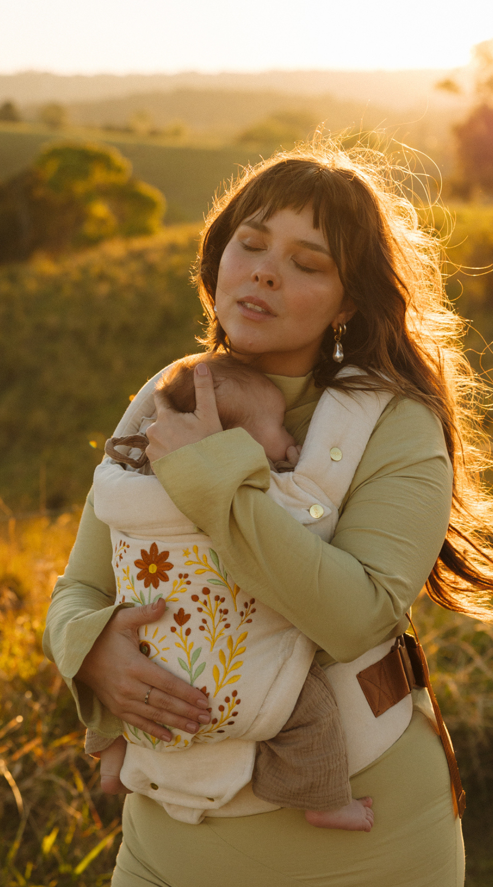 A mother and baby share a moment in a field wearing the vintage white cotton velvet Juni Clip. Featuring a stunning floral seeing eye embroidered design.
