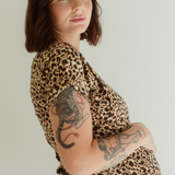A pregnant woman wears the Leopard Print Journey Dress by Chekoh and holds her belly with one hand.