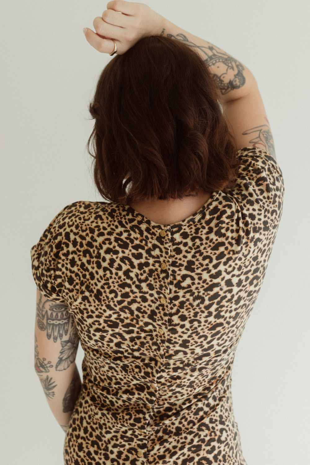 A pregnant woman is wearing the Leopard print Journey Dress by Chekoh, she shows the press stud back details with her arm above her head.