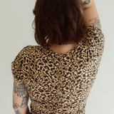 A pregnant woman is wearing the Leopard print Journey Dress by Chekoh, she shows the press stud back details with her arm above her head.
