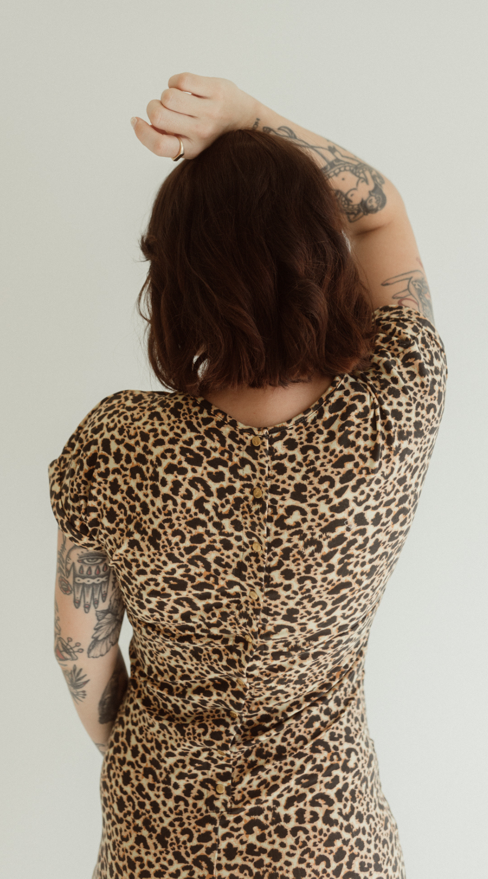 A pregnant woman is wearing the Leopard print Journey Dress by Chekoh, she shows the press stud back details with her arm above her head.