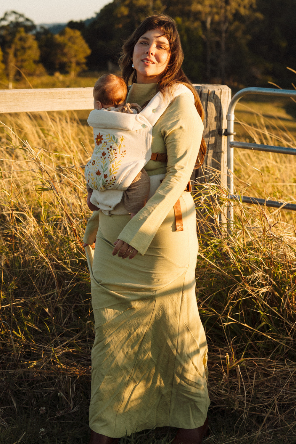 Mother in a field in Australia, wearing the limited edition folk art embroidered Juni Clip Carrier. A cotton velvet base crafted in small batches.