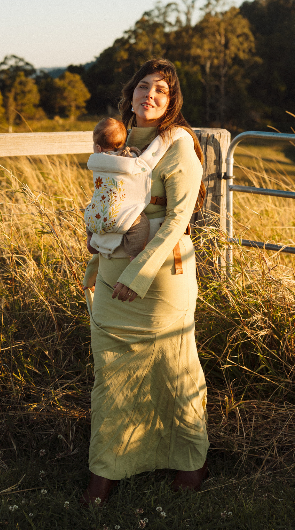 Mother in a field in Australia, wearing the limited edition folk art embroidered Juni Clip Carrier. A cotton velvet base crafted in small batches.