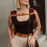 Example of how to use the Chekoh Chest Strap - woman is wearing her child in the Chekoh Clip Carrier in a back carry, using the Chest Strap across her chest for added support.