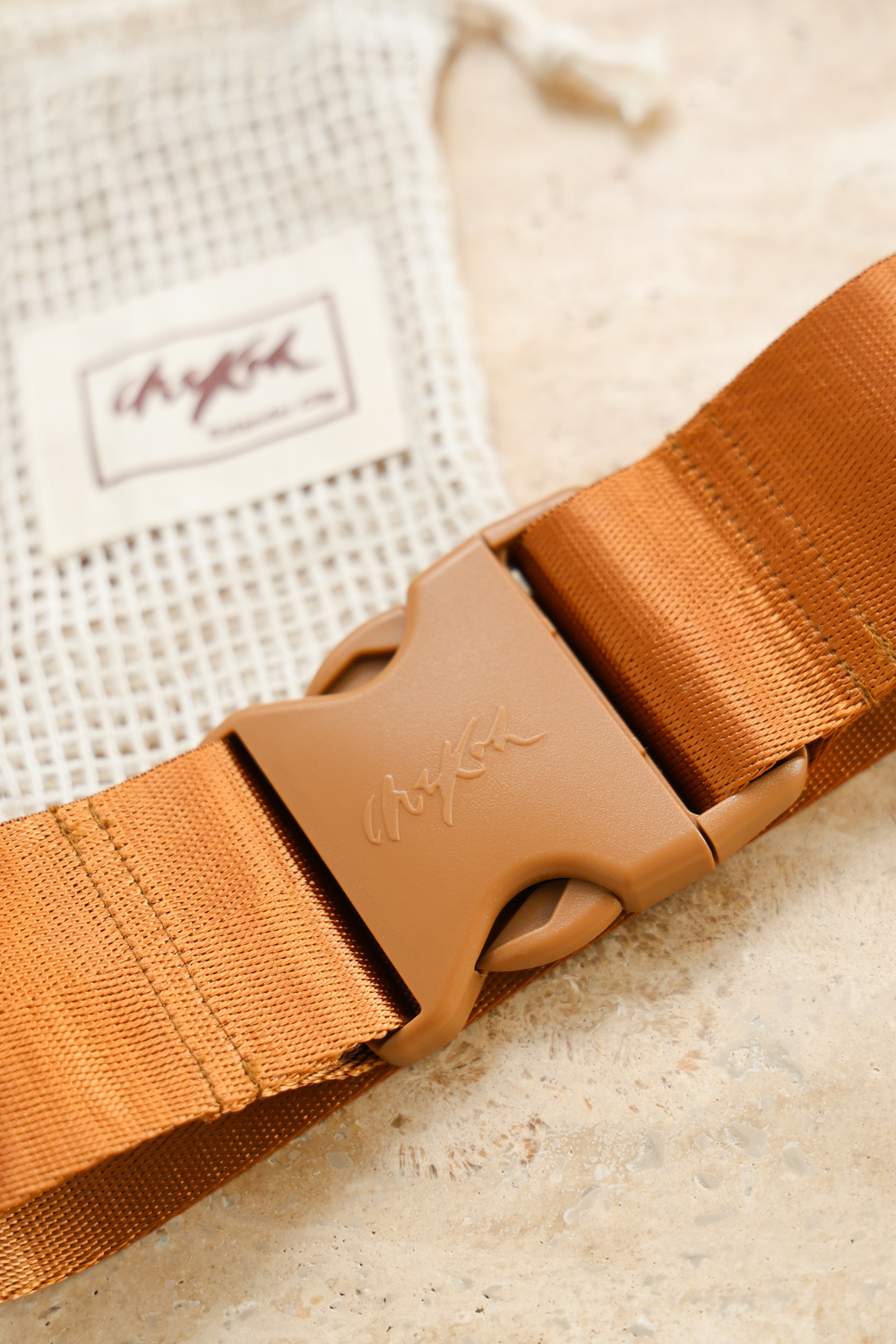 Close up image of the Chekoh Size Extender strap and buckle with a blurred vision of the matching cotton pouch.