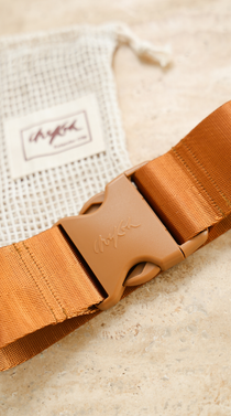 Close up image of the Chekoh Size Extender strap and buckle with a blurred vision of the matching cotton pouch.