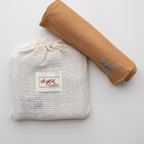 An earthy clay brown Baby Swaddle by Chekoh Baby (Ochre) is sat on a reusable cotton mesh branded wash pouch packaging. 