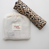 A flatlay image of the Leopard print Baby Swaddle Wrap by Chekoh Baby, rolled up with the cotton wash pouch off centre. You can see the limited edition Leopard print that includes tones of black, tan and cream as well as the logo.