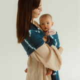A cute baby with fluffy hair is cuddled close in a Chekoh Baby Ring Sling in the tie-dyed print 'Indigo'. 
