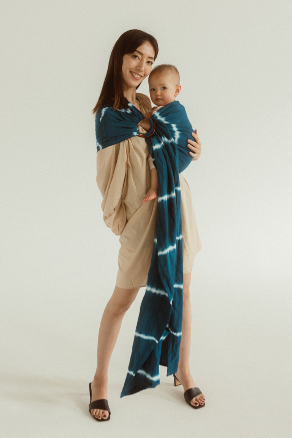 A smiling mother and cute baby are enjoying a cuddle in the Chekoh Baby Ring Sling Carrier in the rich blue and white print 'Indigo'. They are full frame and standing in front of a white background. 