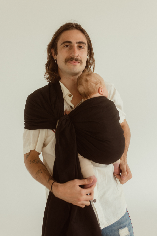 A father and their baby are bonding while wearing the Chekoh Baby Ring Sling in the best-selling Jett black colourway. Baby looks snuggled and sleeping.