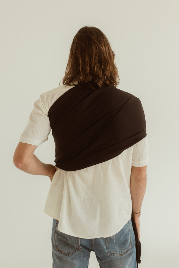 A father wears the Jett Black Chekoh Baby Ring Sling - it can be seen from behind, fanned over one shoulder for even weight distribution. 