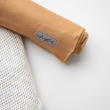 A close up of the Chekoh Baby logo on the Ochre Swaddle Wrap - the Swaddle is a warm earthy brown tone. 