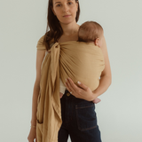 A mother holds her baby close wearing an Australian designed Baby Carrier by Chekoh. It is a Ring Sling Carrier, worn across one shoulder. 