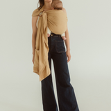 A baby is held close to their mother in a Ring Sling Carrier - it is a soft yellow colour known as Camel, the Rings are visible on the mother's front and a tail of linen and bamboo falls just below her hips revealing a handy pocket too.