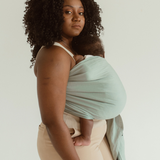 A mother stands side on while wearing her baby in a soft Ring Sling Carrier in Chekoh's signature Teal colourway. A sea inspired green and blue shade.