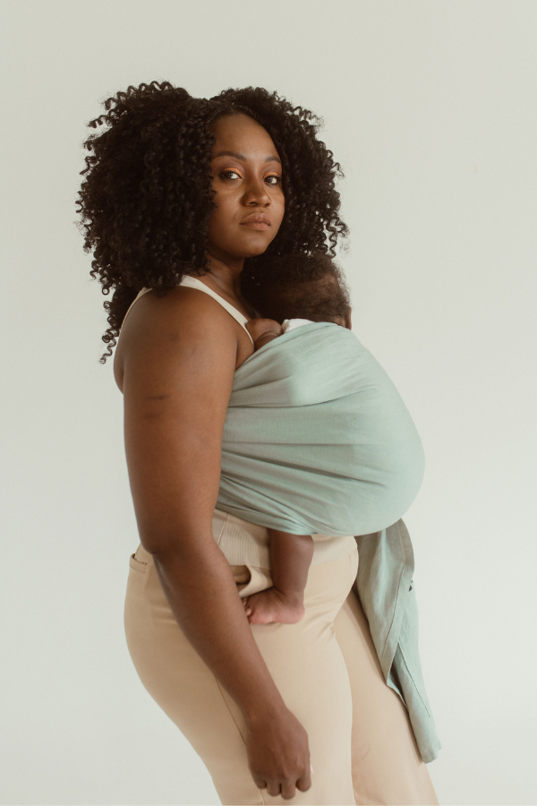 A mother stands side on while wearing her baby in a soft Ring Sling Carrier in Chekoh's signature Teal colourway. A sea inspired green and blue shade.