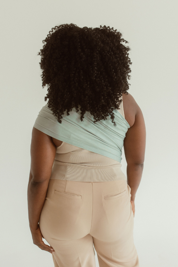 A mother faces away to show off the back of the Teal Ring Sling when worn. The fabric is fanned across her back from one shoulder, down to her opposite side waist. It is a coastal teal tone.