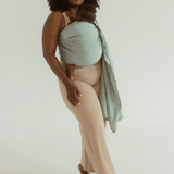A mother is standing on a white backdrop, wearing the Chekoh Baby Ring Sling Carrier in the shade 'Teal'. A coastal green/blue teal tone - perfect for beachy mamas 